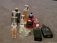 Full view of all 10 perfume and cologne bottles arranged on grey carpet, showing shape, color and relative size.