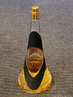 Clear photo of a large conical Rihanna perfume bottle showing amber liquid inside, bottle about half full.
