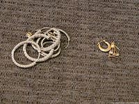Photo of sterling silver hoop earrings on the left and small 14k gold hoop earrings with charms on the right, placed on a brown textured surface.