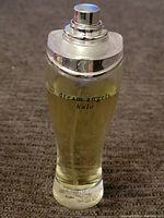 Full view of clear glass perfume bottle with silver cap removed, spray nozzle visible, with yellow perfume liquid at about 80% level inside.