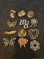 Top down photo showing all 12 brooches arranged in 4 rows on black fabric background.