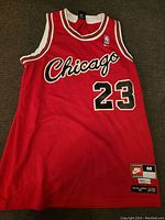 Front view of the red Michael Jordan basketball jersey with Chicago and number 23 on chest; large Nike and sizing tags visible at bottom right.