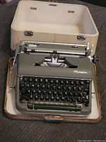 Vintage Olympia typewriter in gray color with QWERTZ keyboard layout packed inside its beige carrying case.