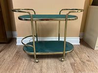 Bar cart side view showing two oval green glass shelves in metal frame on caster wheels.