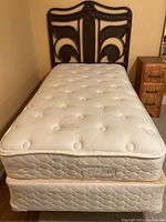 Full view of the single bed with headboard and mattress, showing dark metal frame wicker headboard and white tufted mattress with subtle floral pattern.