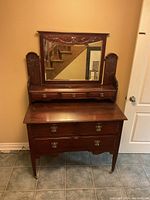 Front view of wooden cabinet with mirror and drawers showing the carved top panel and drawer pulls.