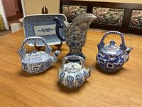 All four ceramic items displayed on wooden surface including three decorative teapots in different shapes and one rectangular serving tray on stand.