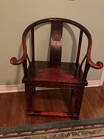Front view of antique Asian-style wooden armchair with curved arms and carved backrest panel.
