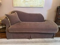 Front and side views of a brown upholstered chaise lounge with one matching cushion against a wall and carpeted floor.