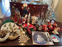 Full table view of assorted Christmas decorations including wreaths, figurines, ornaments, and tableware, showing overall lot contents.