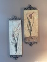Two vertical rectangular framed floral art panels mounted on a wall, showing full pieces and metal scrollwork framing.