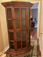 Front angled view of wooden corner display cabinet with glass-panel doors showing grid design