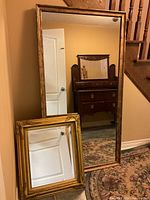 Two mirrors shown together with larger full-length mirror standing and smaller mirror leaning against it.