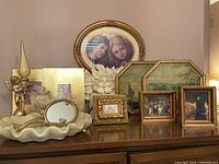 Overall view of assorted decorative items on wooden surface, including framed art, ceramic dish, cherubs, and candle holder.