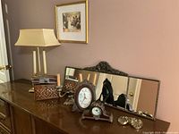 Photo showing a side view of the lot with the lamp, woven box, candelabra, clocks, decorative mirror, and small decorative items arranged on a wooden surface.