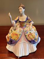 Front view of the Royal Doulton Christine Porcelain Figurine with colorful floral dress and raised arm gesture.