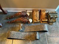 Photo showing two pairs of carved wooden shelving brackets and a pair of metal shelf supports laid on tiled floor.