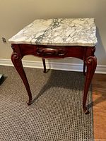 Square side table with white marble top showing prominent grey veining and uneven natural edge, on wooden reddish-brown carved legs and apron.