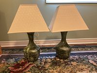 Pair of green ceramic table lamps with beige fabric shades on a floral carpet.