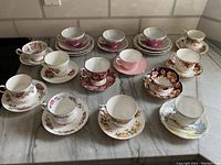 Overview of 13 bone china tea cup and saucer sets on marble tabletop