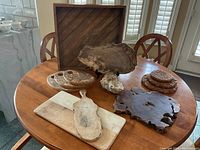 Wide view of all items on round wooden table showing large wooden tray, wooden slab, cork trivets, stone and wood serving boards.