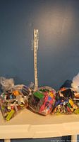 Three clear plastic bags filled with assorted LEGO bricks and minifigures, taken against blue wall background with measuring tape for scale.