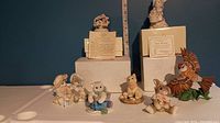 Various Lenox Calico Kitties and other ceramic animal figurines displayed on a white surface against a blue background, some with certificate papers and boxes.