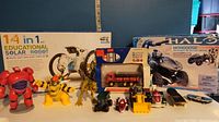 Photo of assorted toys including Big Hero 6 red robot figure, yellow Bowser figure, T-Rex figure, toy vehicles and the 14-in-1 solar robot kit box in background.