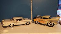 Two die cast collectible muscle cars displayed side by side with a measuring tape showing length of about 13-14 inches.