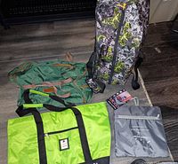 Four large bags as seen from above, including bright green Gloria Vanderbilt tote, green Time duffel with brown straps, gray packable Faraday duffel, and a Lucas rolling duffel bag upright with extended handle.