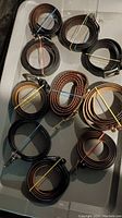 Photo of ten assorted men's belts, rolled and secured with colored rubber bands, displayed on a flat white surface.