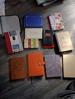 Lot of 11 new hardcover journals, notebooks, address books, photo albums, and padfolio cover arranged on floor.
