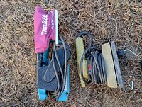 Makita belt sander with attached dust collection bag and Black & Decker finishing sander placed on grass.