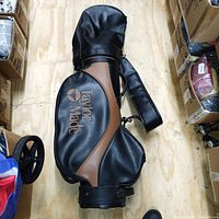 View of the TaylorMade Burner Bubble golf bag lying horizontally on a wooden floor showing the front with logo and padded shoulder strap.