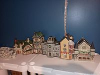 Five vintage ceramic Christmas houses with attached light cords displayed side by side against dark blue wall.