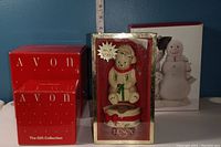Boxed Avon Santa Claus salt and pepper shaker set in red packaging labeled 'The Gift Collection'. Boxed Lenox light-up Christmas bear ornament wearing a Santa hat and scarves, sitting on a red and white base, marked 2003.