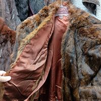Close-up of the inner lining and fur texture of one shorter coat, showing reddish-brown fur with a smooth satin inner lining.