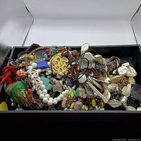 Overhead view of assorted mixed jewelry including beads, chains, pendants, and various styled pieces in a black box.