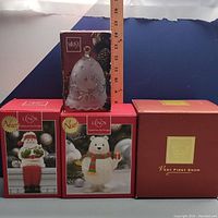 Photo showing all four collectible decorations in their original boxes arranged together with a measuring stick behind the Mikasa bell showing size.