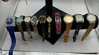 10 untested men's and women's watches arranged side by side on a display stand, showing variety in colors, shapes, and styles.