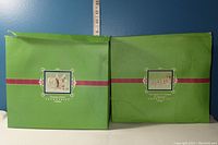 Two green original boxes for Snowbabies figurines with images of the figurines on the face of the box, one depicting two snowbabies in festive attire and the other showing a reindeer and snowbaby group.