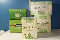 Five original Snowbabies boxes stacked with green and white decorative designs labeled with figurine names.