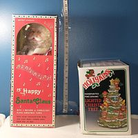 Front and side view of the Santa Claus box with visible musical notes and text about motion and sound features, alongside the boxed ceramic Christmas tree.