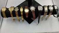 Full view of 10 women's watches displayed on a black cushion, showing mixed metal and leather bands in various styles and colors including gold, silver, brown, and black.