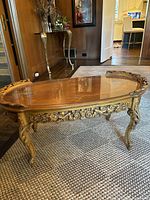 View of antique oval coffee table showing the glass top, inlaid wood design, and carved wood legs in room setting.