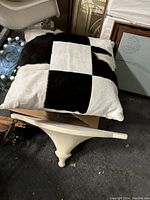 Black and white checked hair on hide euro pillow and large plaster shelf with a wide, shallow design and tapered central support.