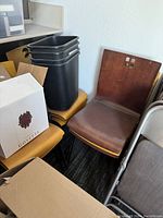 Six solid wood dining chairs including four yellow wood chairs and two reddish-brown wood chairs in corner with some dust and light wear visible.