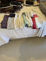 Photo showing nine tennis skirts and one tennis dress laid out on the bed. Skirts vary in color and pattern, mostly white with colorful waistbands and some solid pastels and stripes.