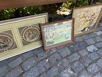 Three framed prints leaning against a step outdoors on cobblestone, showing all three frames and various subjects.