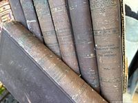 Seven vintage brown hardcover books stacked side by side showing spine titles and wear.